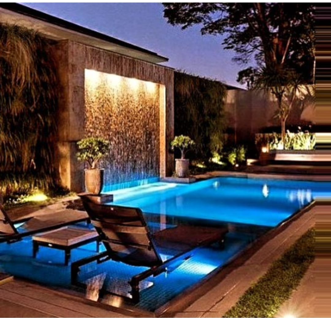 Alberca iluminada junto a terraza y jardín